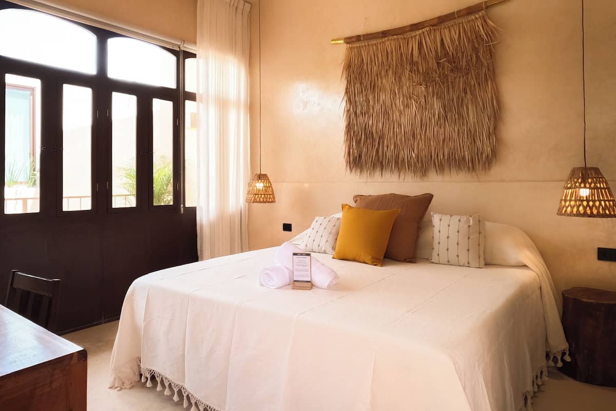 A bedroom with a large bed, a wooden headboard, a hanging woven wall decoration, and two pendant lights.