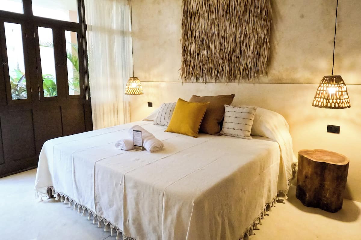 A large bed with a white bedspread, multiple pillows, and a bedside table with a lamp.