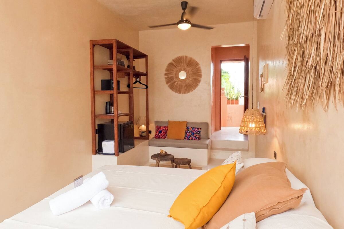 A bedroom with a bed, a wooden shelf unit, a ceiling fan, and a view of the outside.