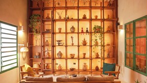 A cozy room with a wooden bench, shelves with pottery, and a window with green shutters.