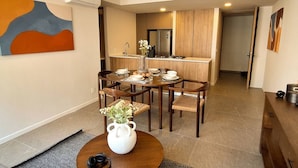 Un espace repas moderne avec une table et des chaises en bois, un vase rempli de fleurs et, au fond, une cuisine.