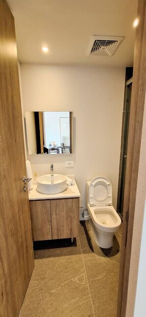 Een kleine badkamer met een rond wastafel, toilet en spiegel boven het wastafel.