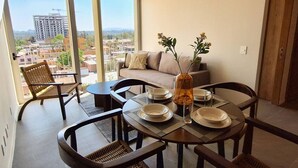 A dining area with a view of a cityscape, a sofa, and a vase with flowers.