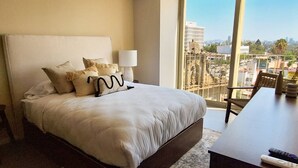 A hotel room with a large bed, a desk, and a view of the city.