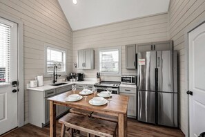 A compact kitchen with white cabinetry, a stainless steel refrigerator, and a wooden dining table set for four. - Cozy Current Lake Cabin! +Pet Friendly +Game Loft! (Sevierville)