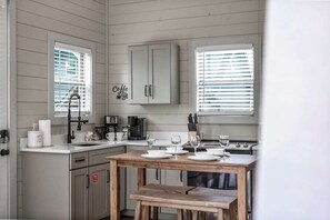 A kitchen with a wooden table set for dining, a coffee machine, and a cabinet with a sign. - Cozy Current Lake Cabin! +Pet Friendly +Game Loft! (Sevierville)