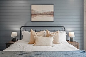A bed with a headboard, two bedside tables with lamps, and a wall-mounted painting.