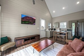 A modern kitchen with a dining area, a large flat-screen TV mounted on the wall, and a built-in bench with storage.