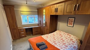 A bedroom with a bed, wooden wardrobe, and a window with a view of buildings. - 3 bedroom spacious home Parking and WiFi sleeps 5 (Bexleyheath)