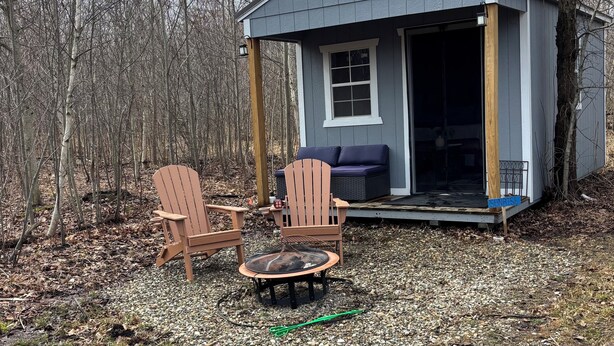 Une petite cabane avec une véranda, deux fauteuils Adirondack, une table ronde et un espace clos.