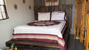 Une chambre avec un lit en bois, une fenêtre, une œuvre d’art accrochée au mur et une chaise en bambou.