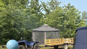 Une tente, un quad bleu et une remorque, le tout situé dans une zone herbeuse, avec des arbres en arrière-plan.