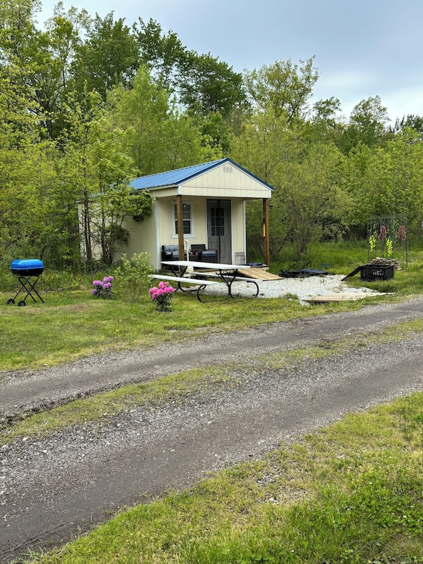 A small, single-story house with a blue roof, a porch, and a picnic table. - Cabin 1 The Sunrise Patio (Geneva)