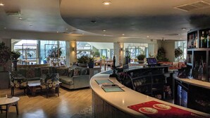 Un hall d’hôtel spacieux, doté d’un comptoir d’accueil incurvé, de coins salon et de grandes fenêtres laissant entrer la lumière naturelle.