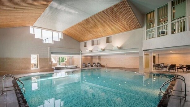 Une piscine intérieure à l’eau claire, entourée de murs carrelés et surmontée d’un plafond en bois.