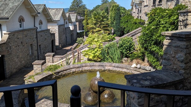 A courtyard with stone buildings, a small water feature, and lush greenery. - Spacious house, high in the hills, stunning views, on-site indoor pool, bar, gym (Keswick)