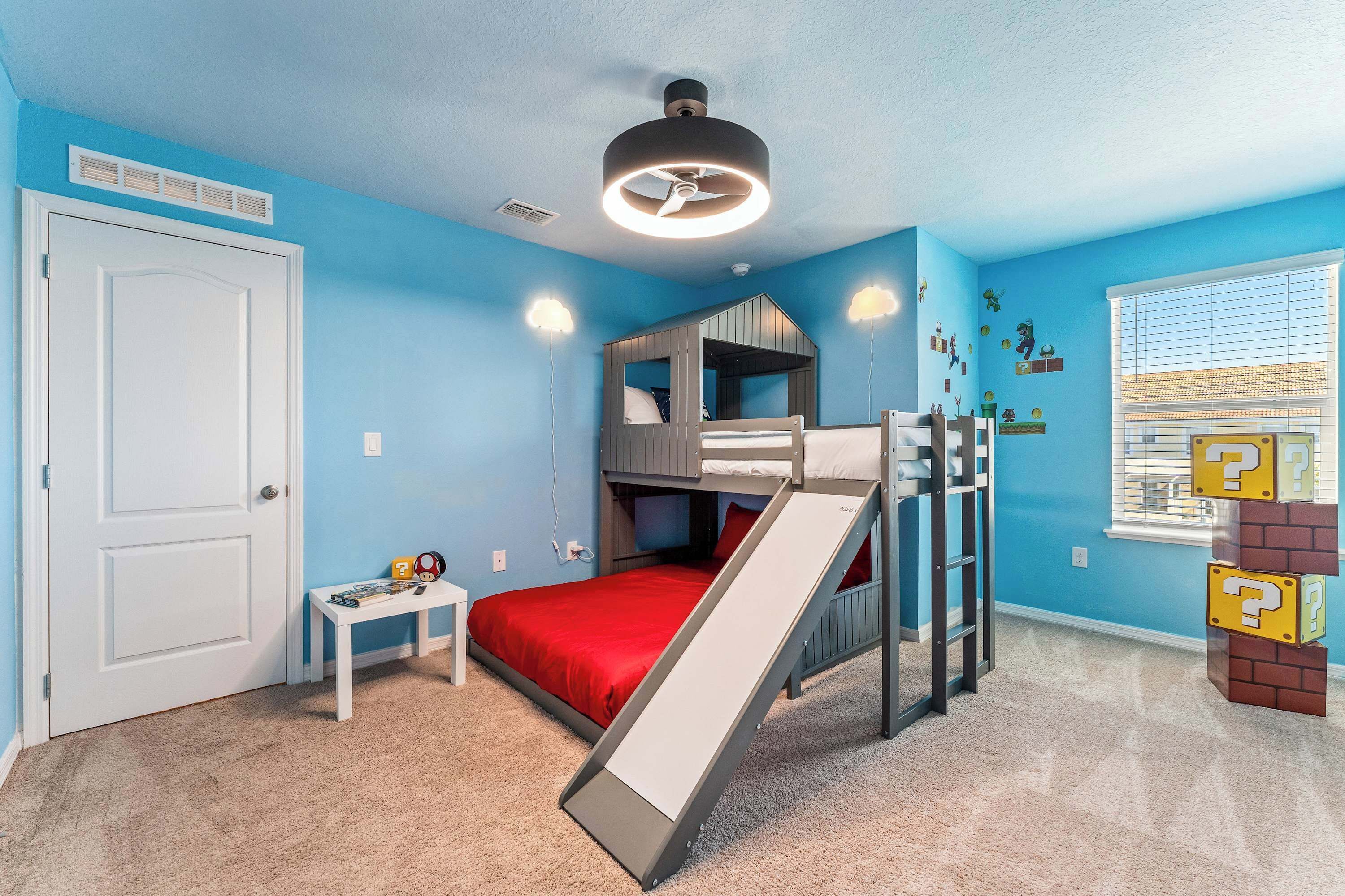 Une chambre d’enfant avec des lits superposés, un toboggan et une fenêtre avec des stores.