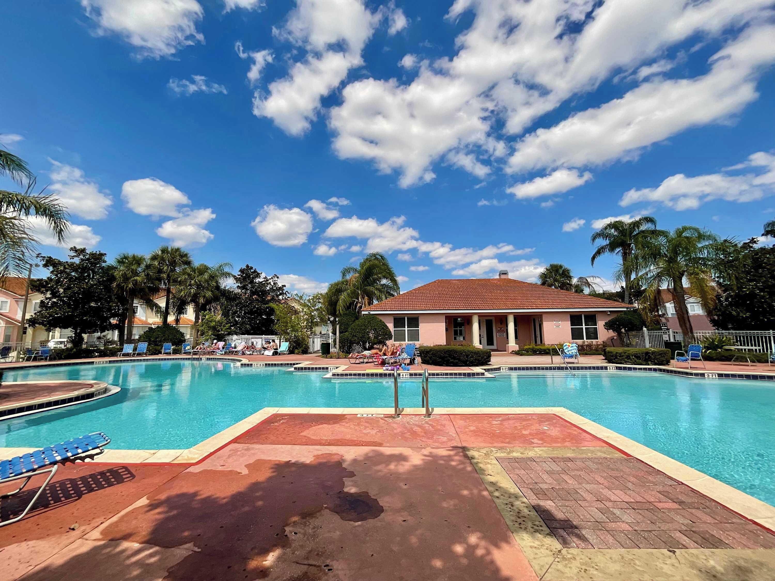 A swimming pool with lounge chairs, palm trees, and a building with a red roof.
