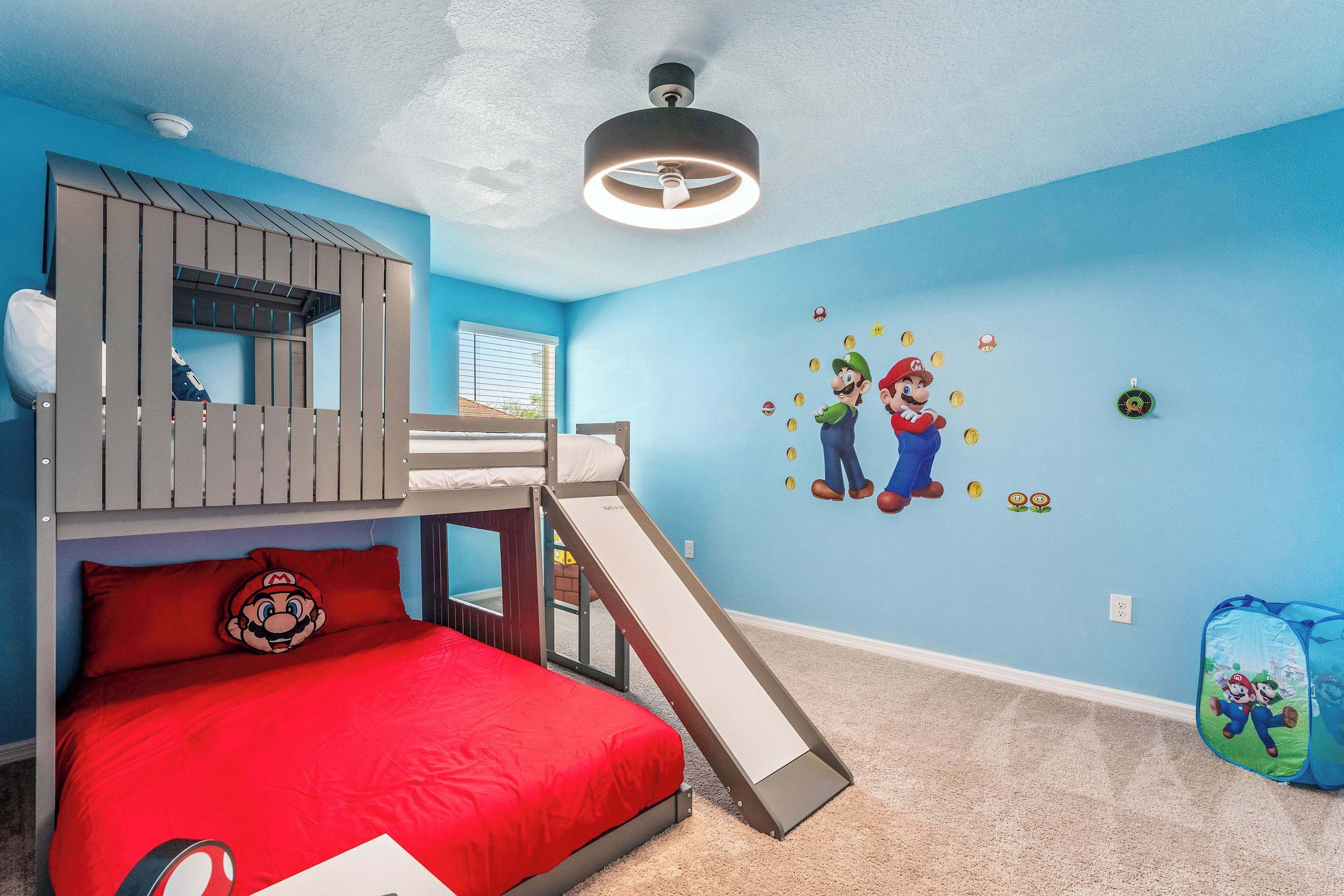 Un dormitorio con literas, un tobogán y pegatinas de pared con temática de Mario.