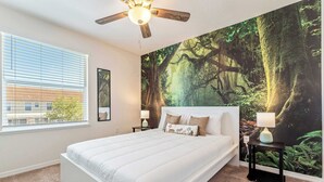 Ein Schlafzimmer mit einem großen Bett, einem Deckenventilator, einem Fenster mit Jalousien, einem Nachttisch mit Lampe und einem Wandgemälde von einem Wald.