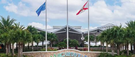 The entrance of Margaritaville Resort with three flags, palm trees, and a modern building structure.