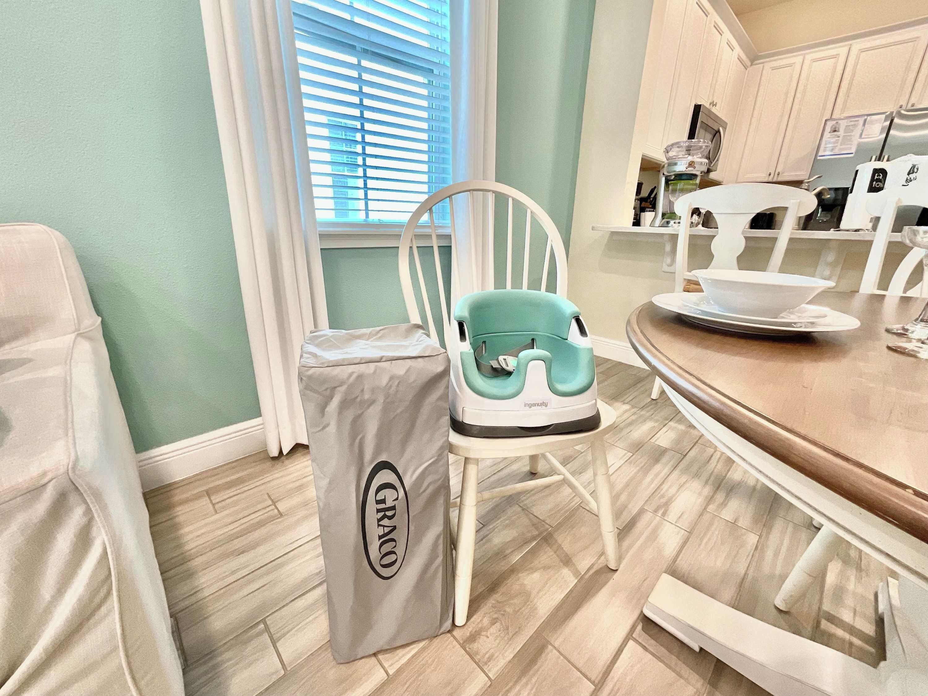 A kitchen with a teal-colored high chair, a white chair, and a dining table with a white plate and bowl.