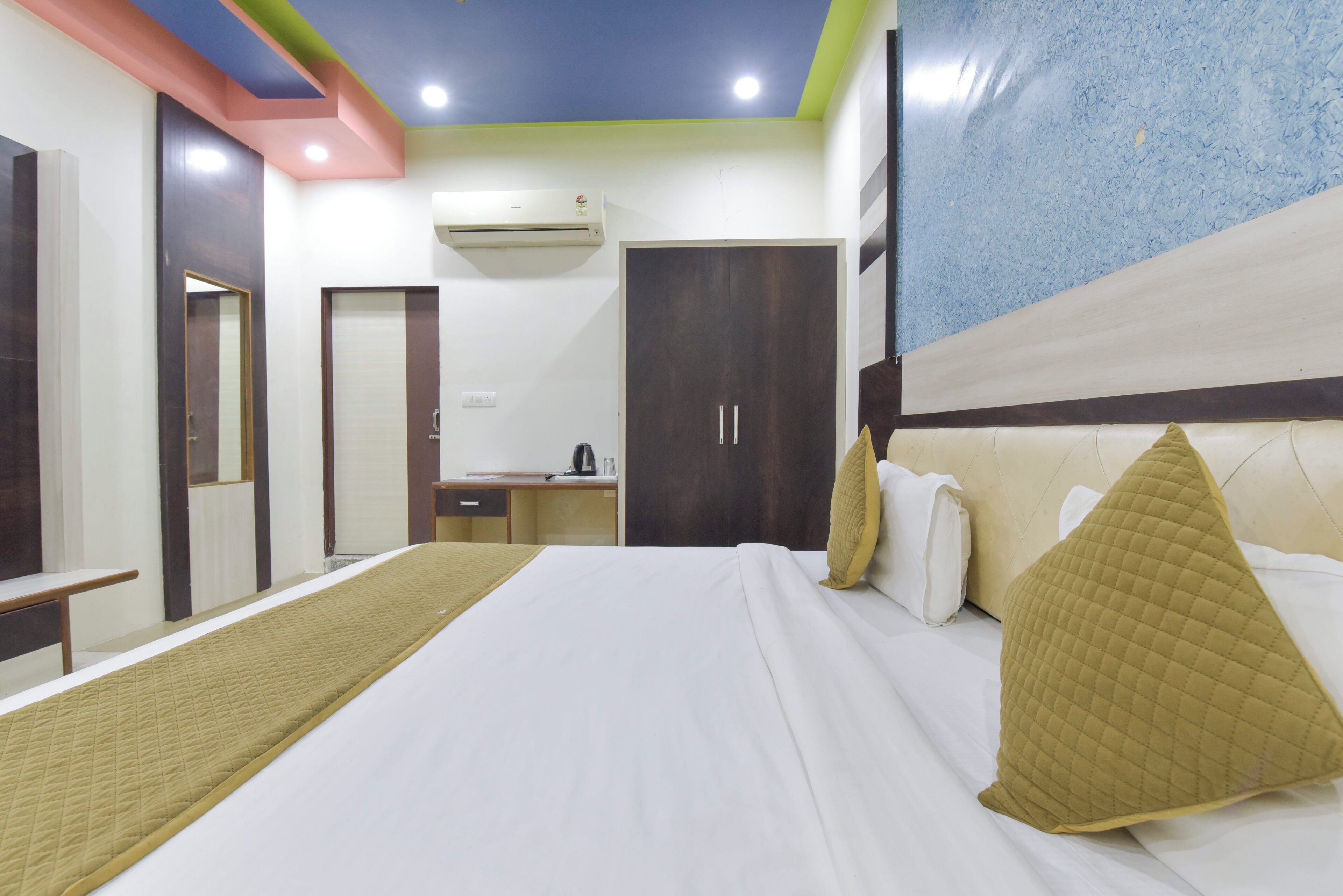 A hotel room with a large bed, a desk, an air conditioner, and a wardrobe.