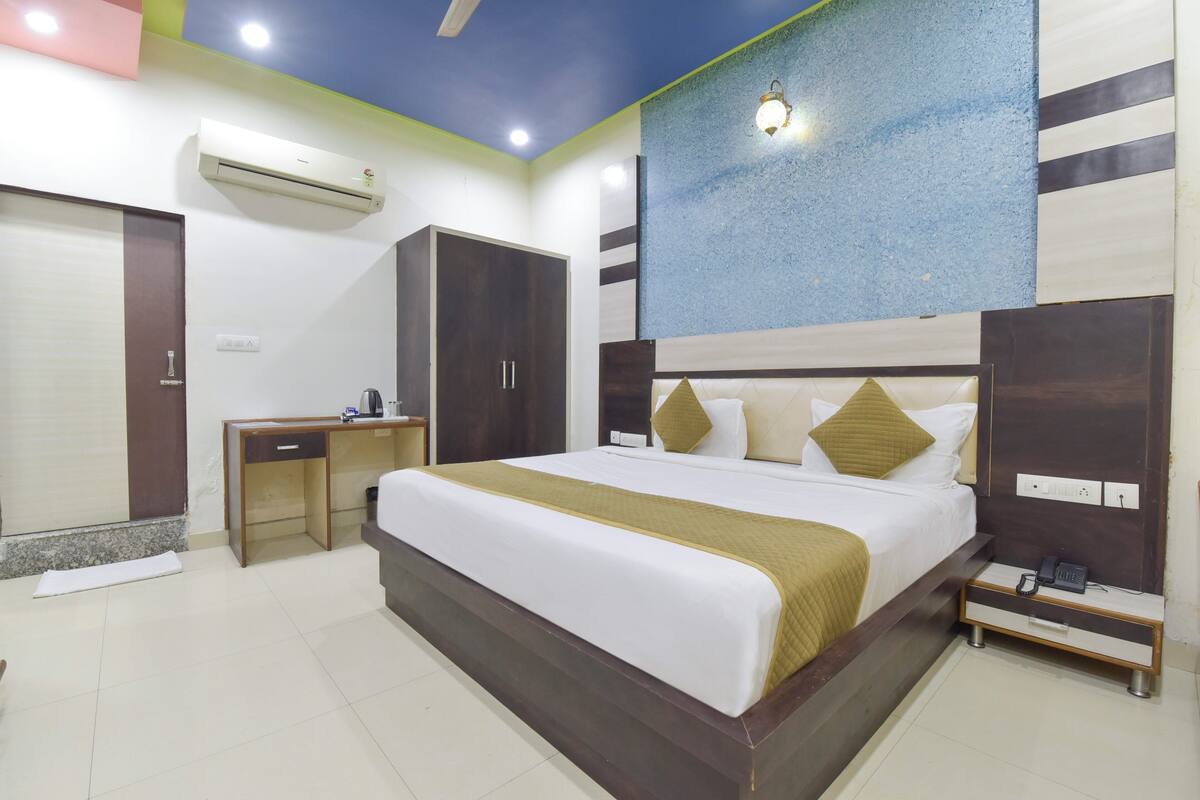A hotel room with a large bed, a desk, a wardrobe, and an air conditioning unit.