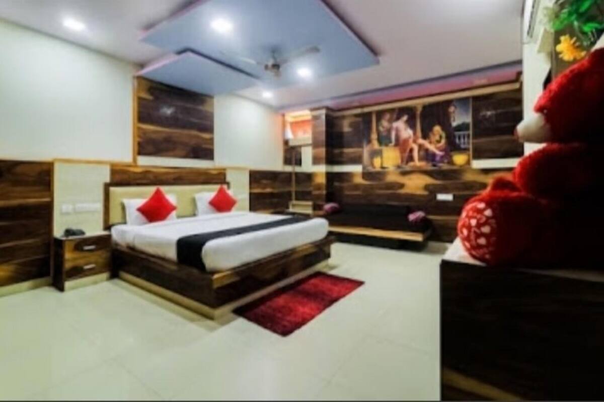 A bedroom with a bed, nightstands, a red rug, and a large teddy bear.
