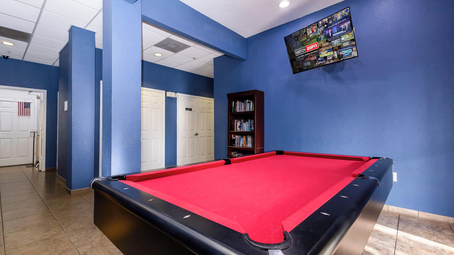 Une table de billard recouverte d’un drap de feutre rouge, une bibliothèque et un téléviseur fixé au mur diffusant les programmes d’ESPN.