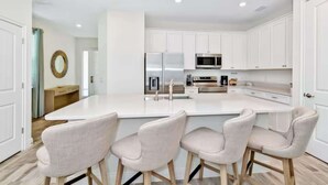 A modern kitchen with white cabinetry, stainless steel appliances, and a central island with bar stools. - Pistachio Palace Sleeps 10! (Kissimmee)