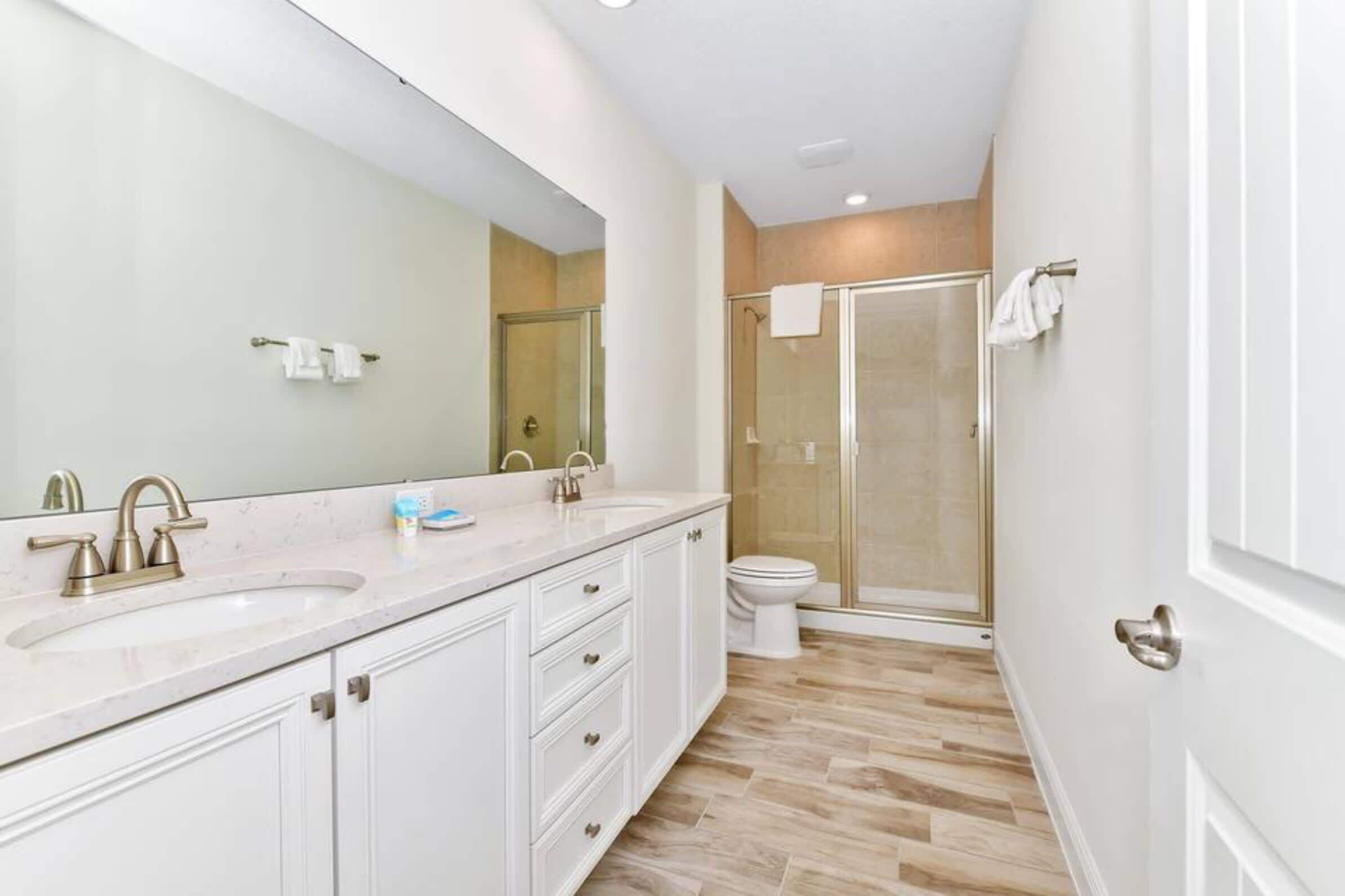 A modern bathroom with a large mirror, two sinks, a toilet, and a glass-enclosed shower.