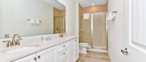 A modern bathroom with a large mirror, two sinks, a toilet, and a glass-enclosed shower.