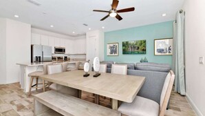 A modern kitchen with white cabinets, a dining table with benches, and a ceiling fan. - Pistachio Palace Sleeps 10! (Kissimmee)