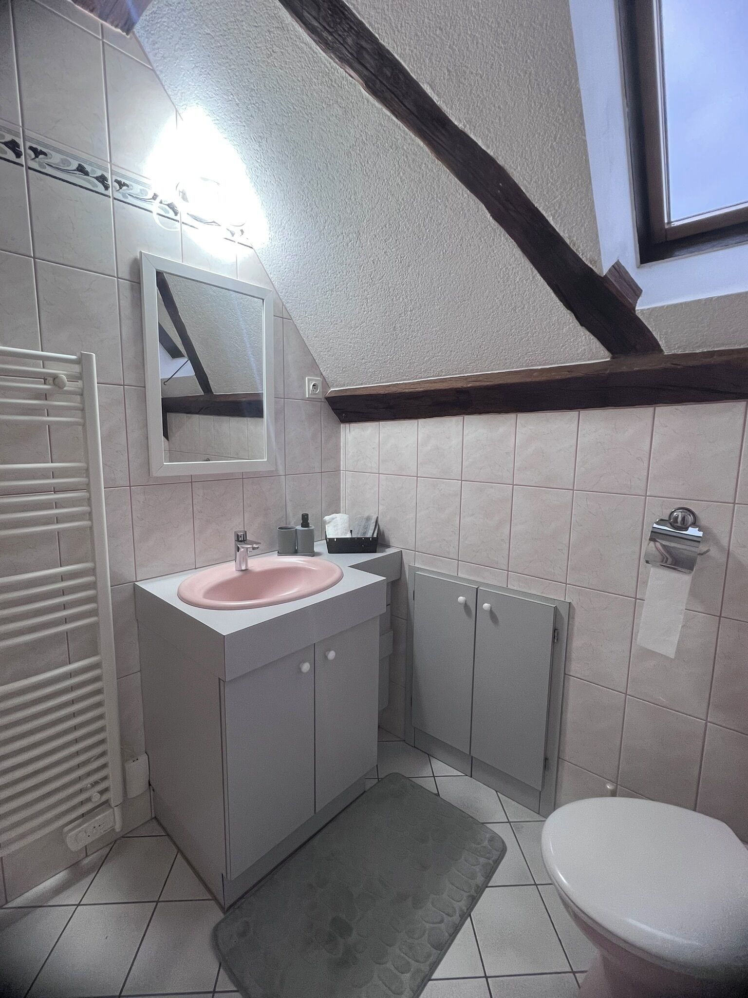 A bathroom with a white sink, mirror, and toilet. There is a towel rack and a small window above the toilet.