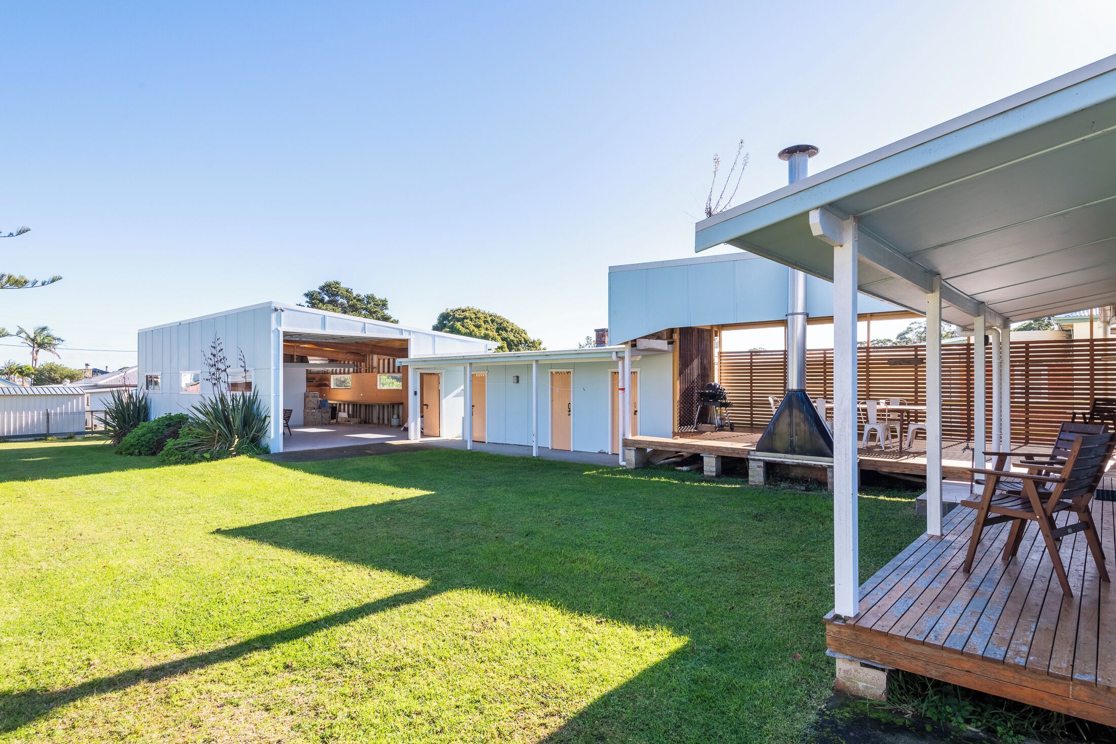 Een modern buitenterras met een houten dek, een barbecue en een zithoek met stoelen en tafels.