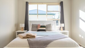 A neatly made bed with pillows and a blanket, two bedside tables with lamps, and a window with curtains. - South Cantina * Currarong π€πΌππ½π¨βπ©βπ§βπ§ππ©²οΏ½ (Currarong)