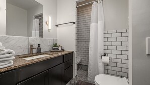 Une salle de bain moderne avec un comptoir en marbre, des meubles noirs, des toilettes blanches et une douche avec un rideau blanc.