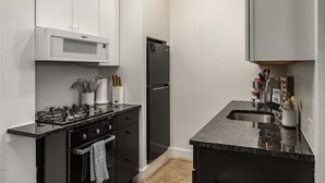 Une cuisine de taille réduite équipée d’une cuisinière à gaz, d’un four, d’un four à micro-ondes et d’un réfrigérateur noir.