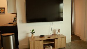 Un salon moderne avec un téléviseur à écran plat fixé au mur, une console en bois ornée d’une plante, une télécommande et un objet décoratif.