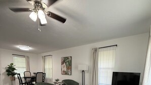 A living room with a ceiling fan, a television, a sofa, and a dining area with chairs and a table. - Charming 2-bedroom house with WiFi, AC in fantastic Downtown Lake City (Lake City)