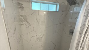 A bathroom with a glass-enclosed shower, marble walls, a patterned shower curtain, and a small window. - Charming 2-bedroom house with WiFi, AC in fantastic Downtown Lake City (Lake City)
