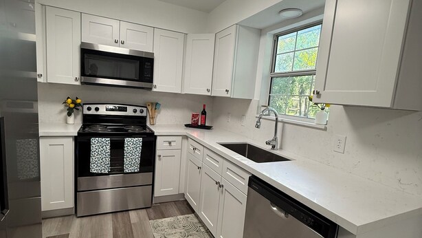 A modern kitchen with white cabinets, stainless steel appliances, and a window providing natural light. - Charming 2-bedroom house with WiFi, AC in fantastic Downtown Lake City (Lake City)