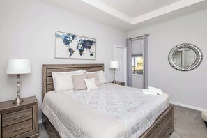 A bedroom with a large bed, two bedside tables, a world map artwork, a round mirror, and a door leading to another room. - Silver Lining Luxury for 10! (Haines City)