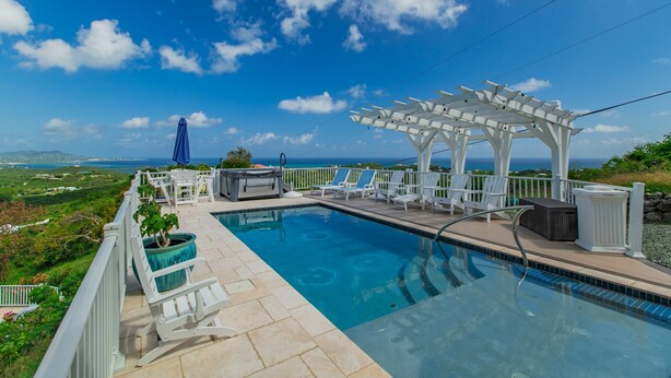 A pool area with a pergola, lounge chairs, and a view of the ocean. - Caribbean Escape - Sunset Palms! (Christiansted)