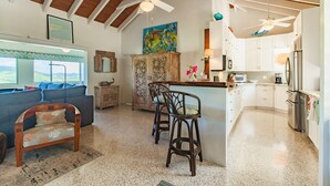 A spacious living area with a large window, a wooden ceiling, a bar area, and a kitchen with white cabinets and stainless steel appliances. - Caribbean Escape - Sunset Palms! (Christiansted)
