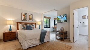 A bedroom with a large bed, a wooden nightstand, a desk, a chair, and a television on the wall. - NEW LISTING: Ka’anapali Royal K303 2BR – Ocean Views, Pool, Walk to Golf & Beach (Lahaina)
