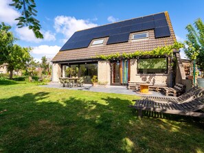 A house with a sloped roof, solar panels, a covered patio, and a garden.