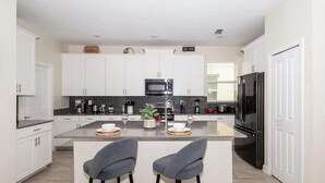 Una cocina moderna con armarios blancos, una isla central, dos taburetes de bar y un refrigerador negro.