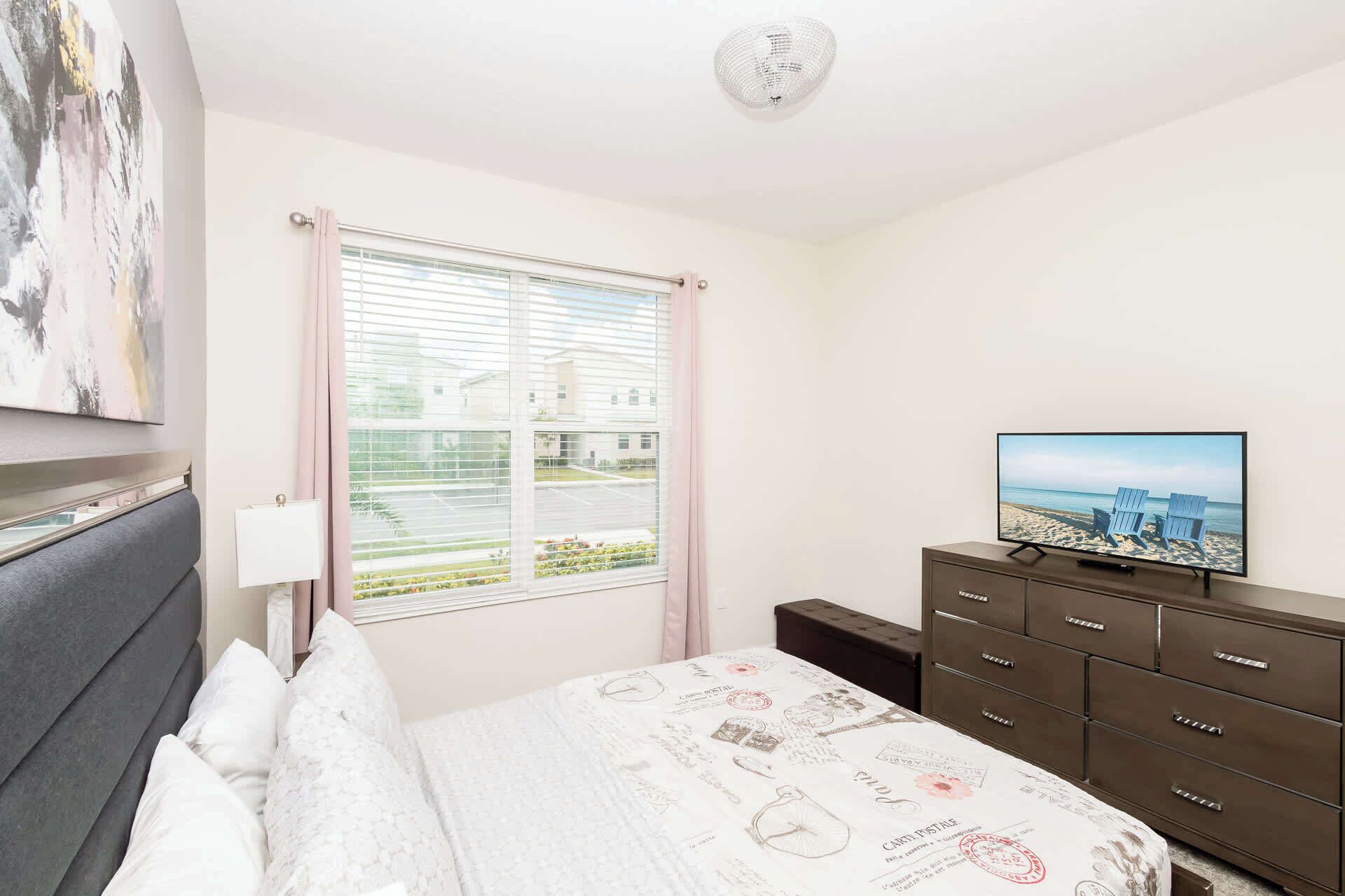 A bedroom with a bed, a dresser, a television, and a window with blinds.